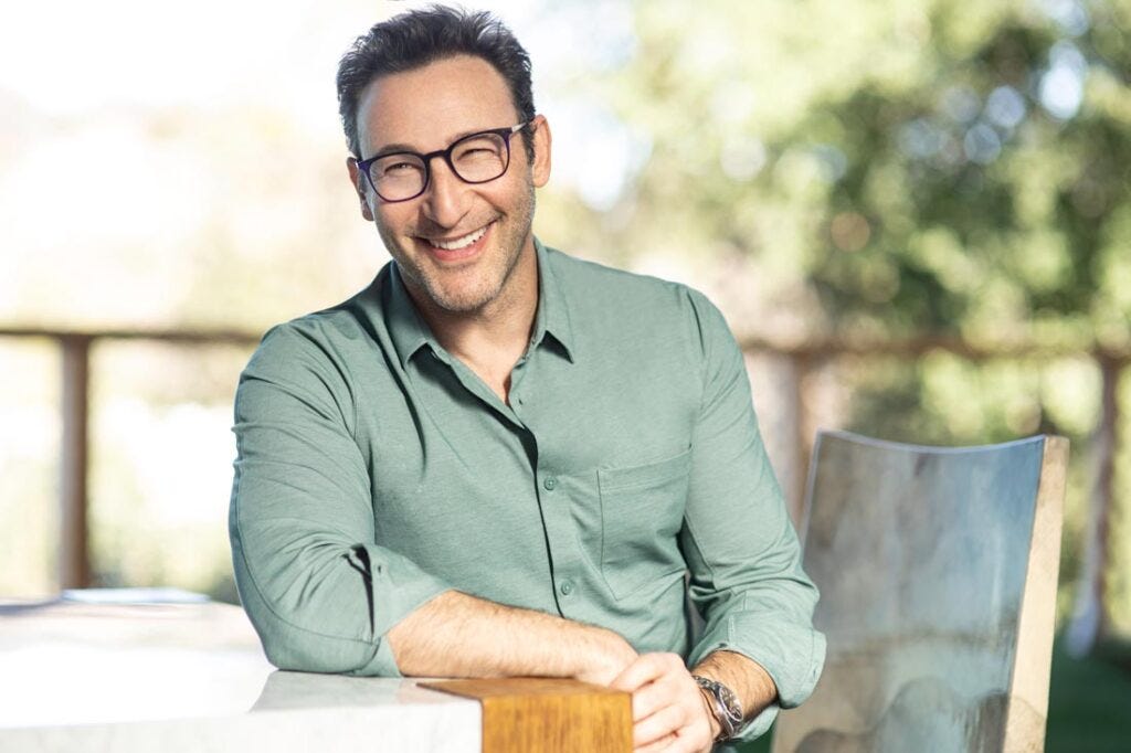 Simon Sinek, the influential leadership author and speaker, engages an audience on stage during a professional conference, gesturing animatedly with a microphone in hand while dressed in a dark suit, embodying his philosophy of purpose-driven inspiration.
